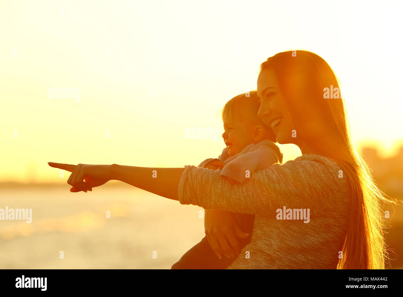 Happy mother and kid son looking away and pointing horizon at sunset Stock Photo