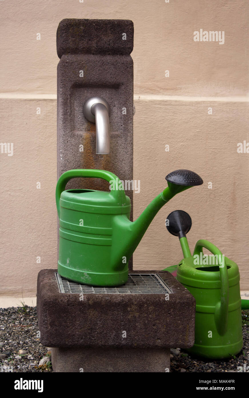 Two green watering cans at an outdoor water faucet Stock Photo