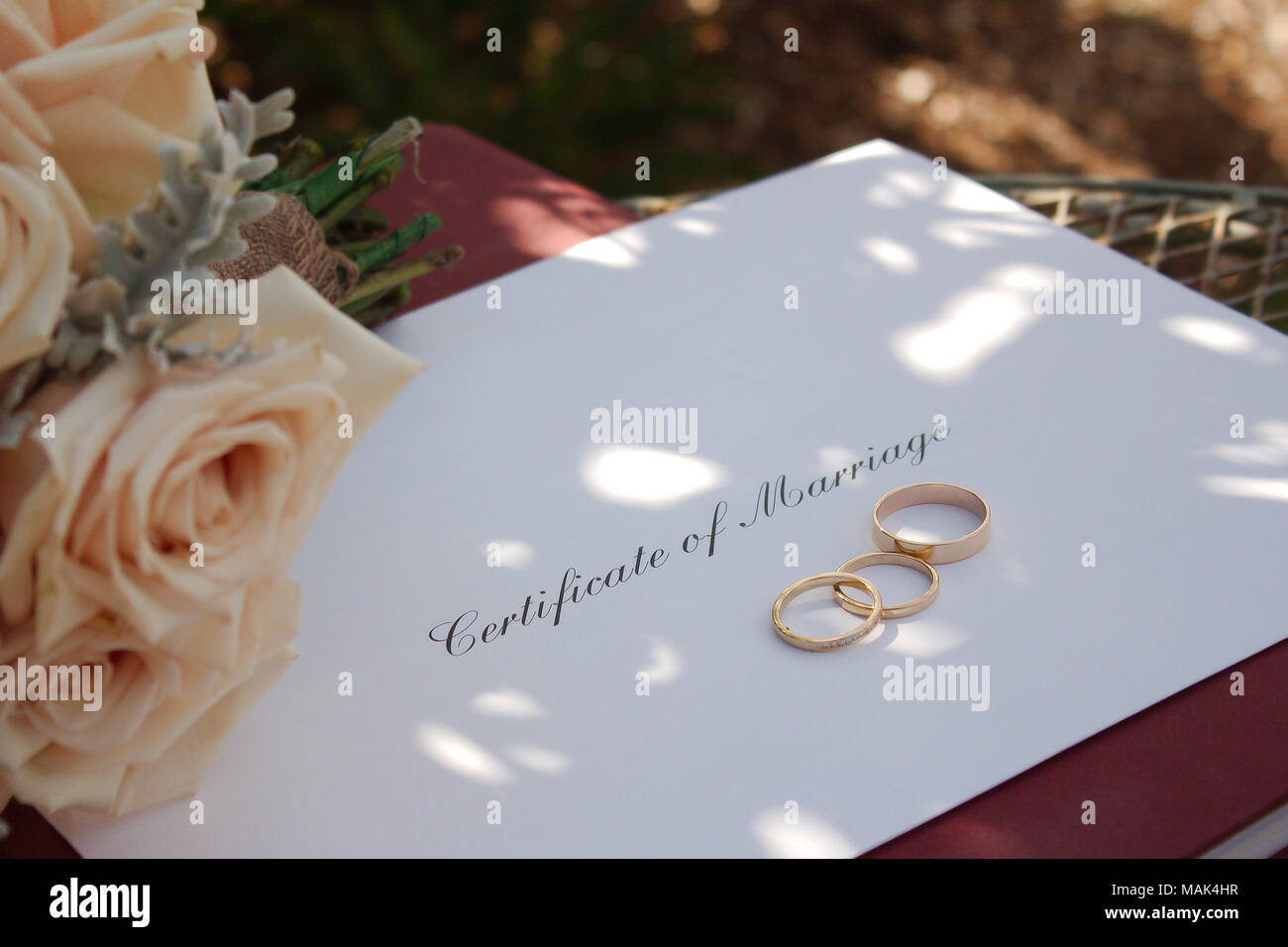 An envelope with 'Certificate of Marriage' written on it sits on the Marriage Register . Along side it is the Brides Bouquet & the wedding rings. Stock Photo