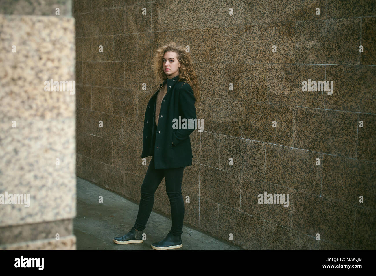 city portrait of a young woman with curly hair dressed in a black coat ...