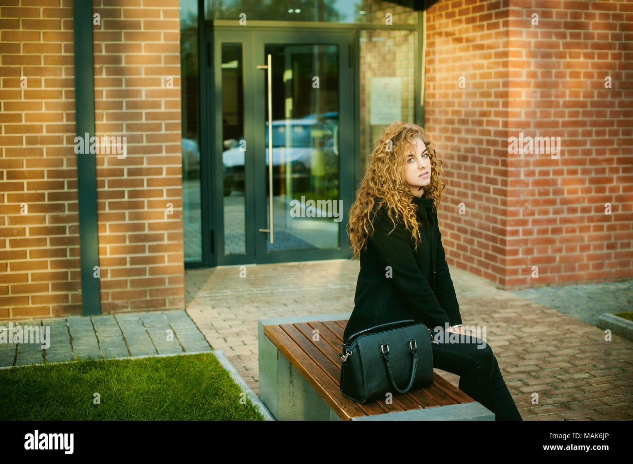 city portrait of a young woman with curly hair dressed in a black coat ...