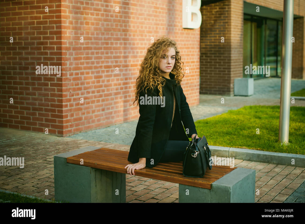 city portrait of a young woman with curly hair dressed in a black coat ...