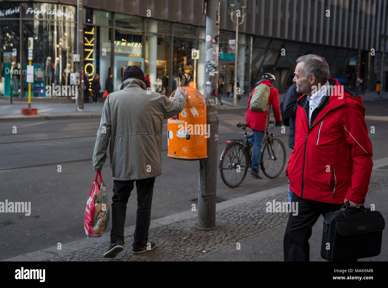 A pedestrian looks at a man taking something out of a bin in Berlin, Germany. Stock Photo