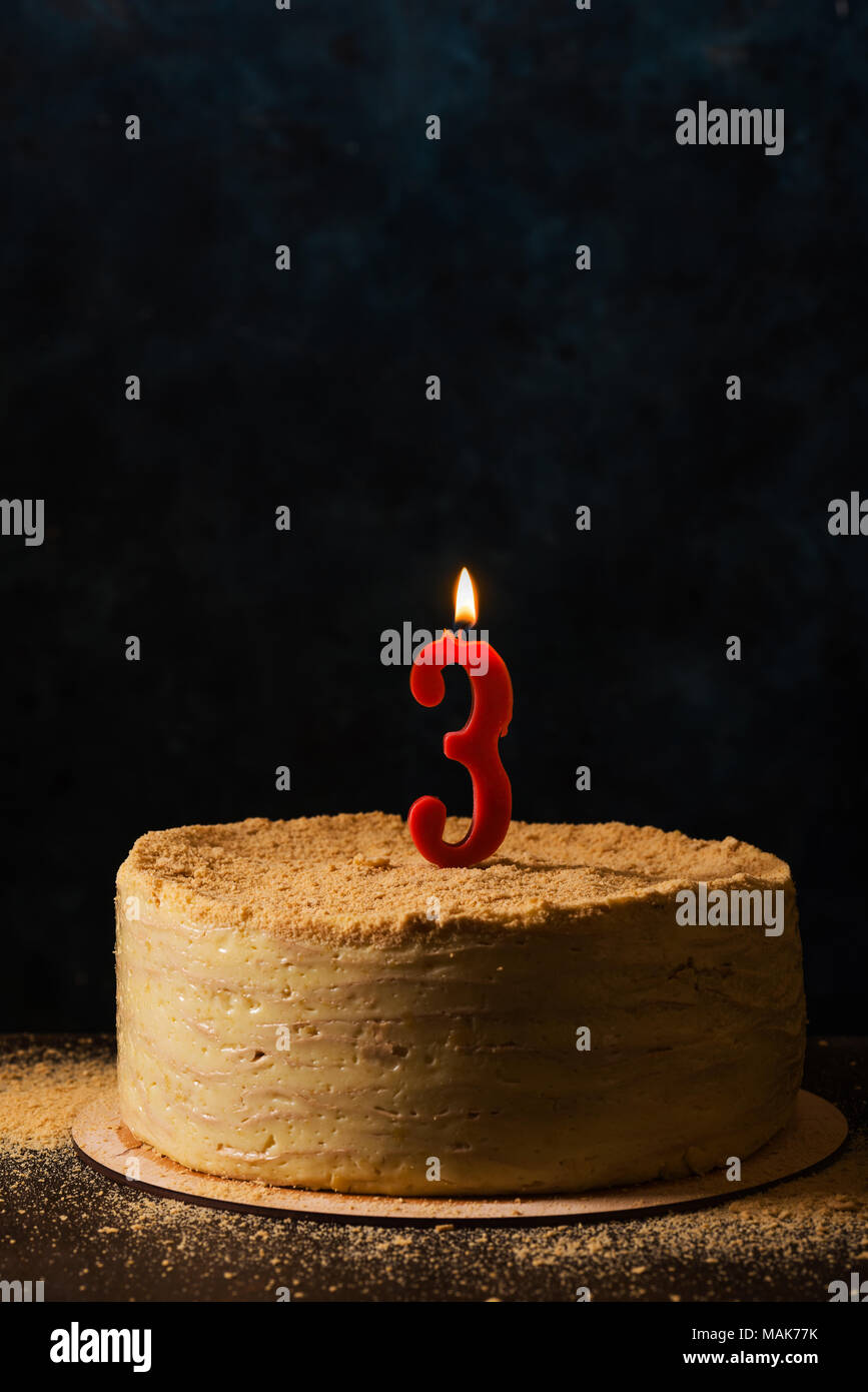 Traditional napoleon cake with threeshaped candle. Still life in dark