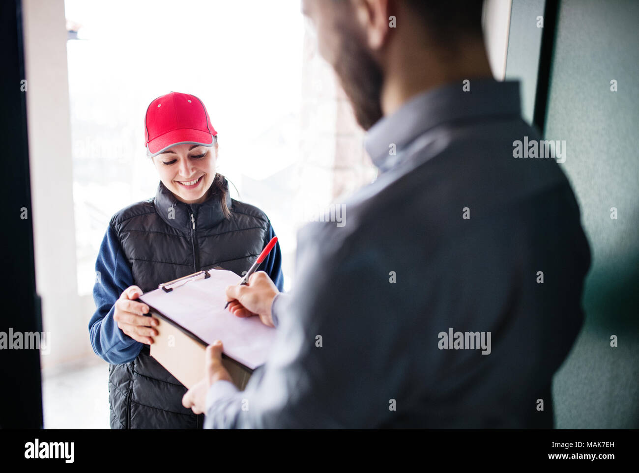 A man receiving parcel from delivery woman at the door. Stock Photo