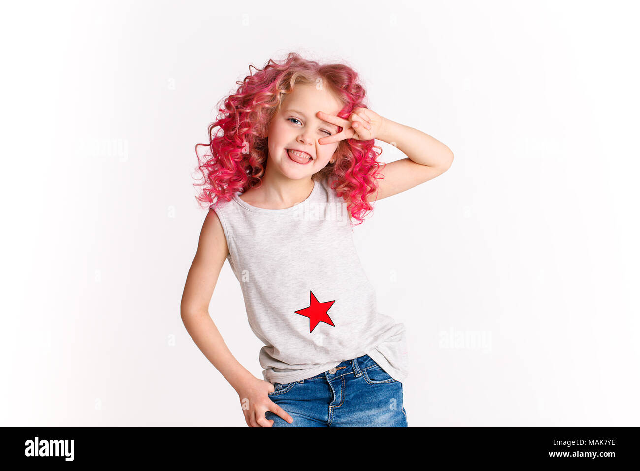 Colored wavy hairs. Little modern hipster girl in fashion clothes, make peace by her hand. Studio Stock Photo