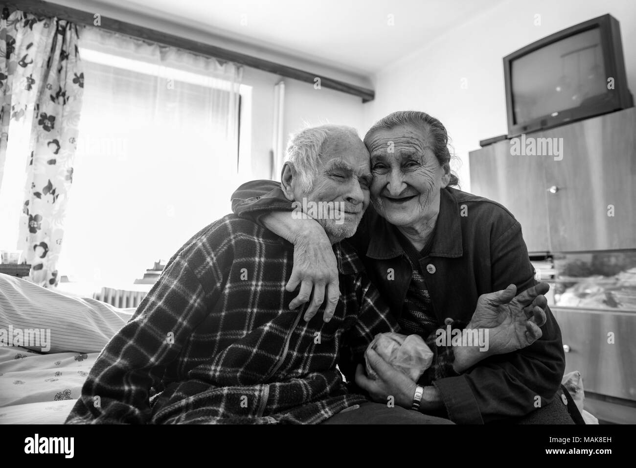 Cute 80 plus year old senior married couple hugging and smiling portrait.  Black and white waist up image of happy elderly couple sitting on a bed  Stock Photo - Alamy