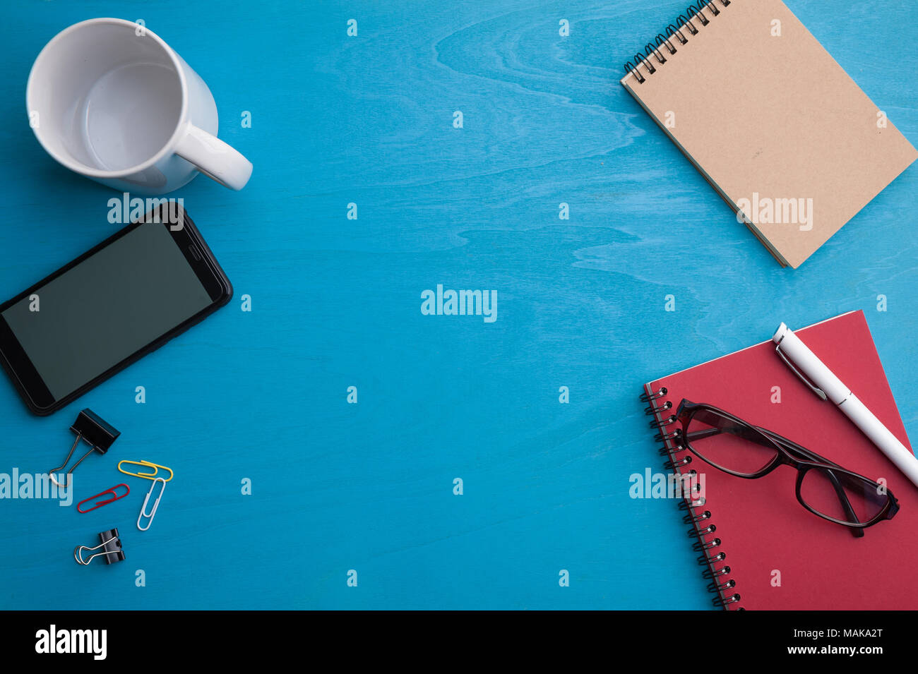 Smart phone, small notebook, glasses, and coffee cup on blue wood table. background with blank area for text or message. Stock Photo
