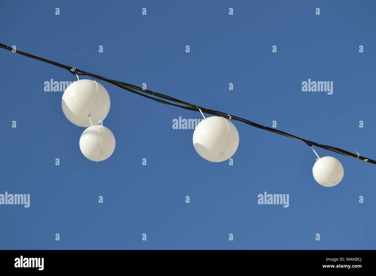 White garland balloons oscillate in the wind against blue sky and clouds, peaceful landscape Stock Photo