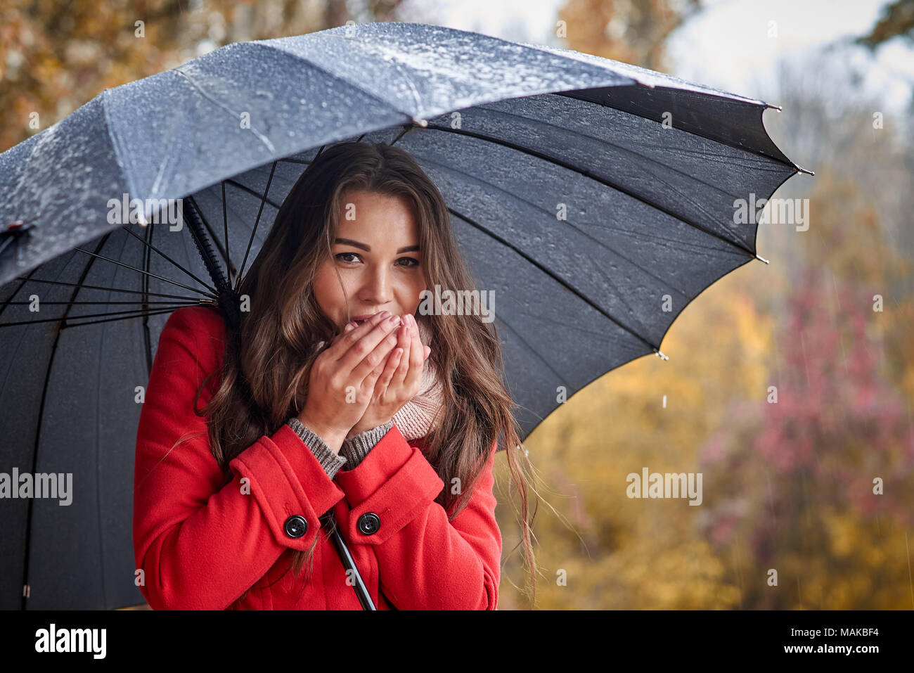 The girl under the umbrella warms her hands with her breath Stock Photo