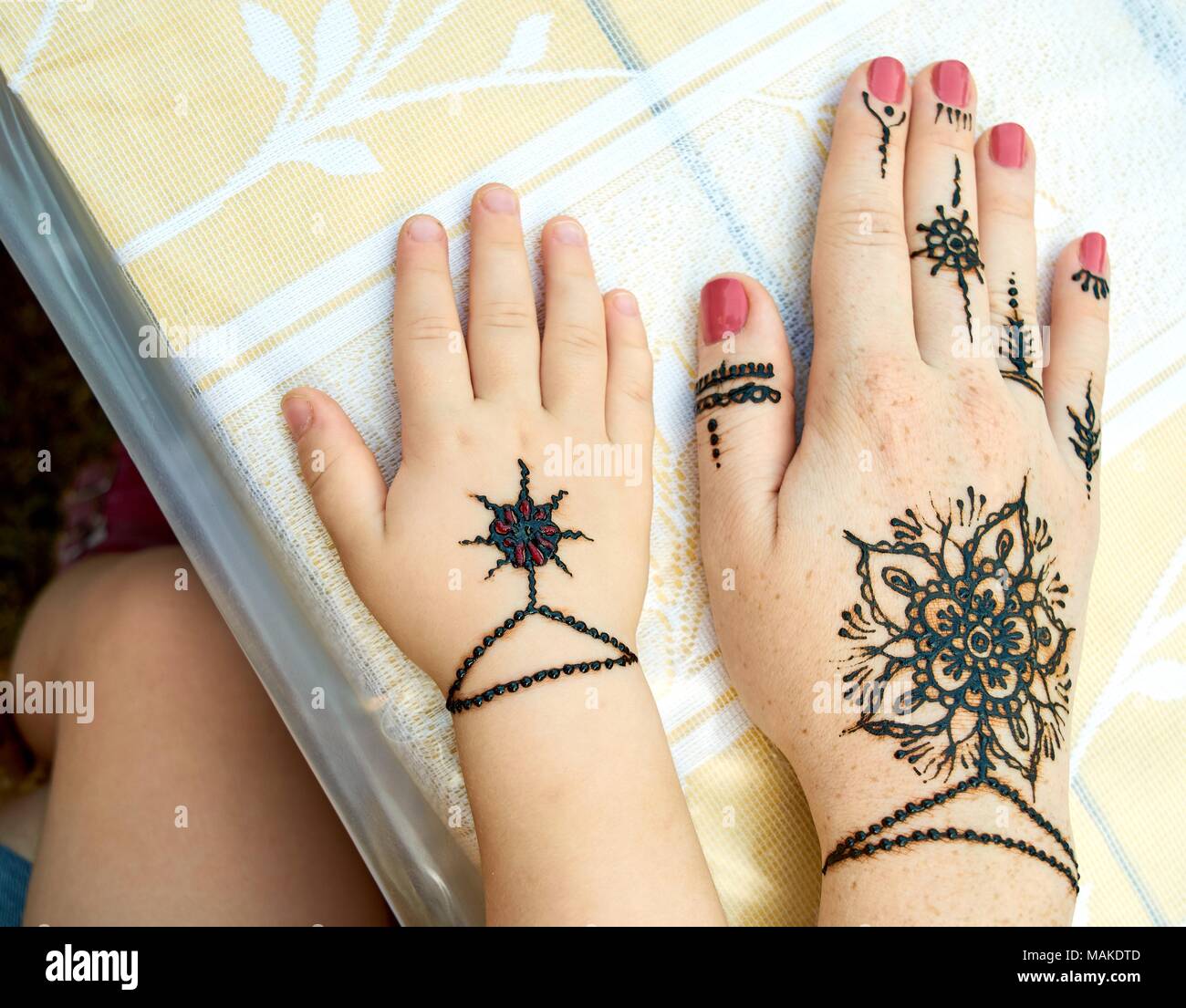 Hands of a mother and child with a traditional indian black flower tattoes on the table outdoors close-up Stock Photo