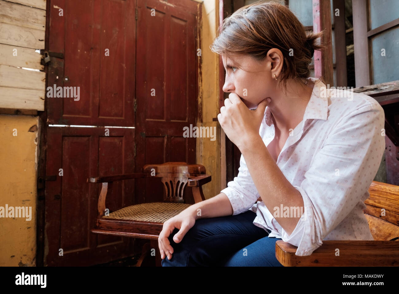 Profile of caucasian young woman sitting in strange place with shabby old walls and thinking Stock Photo