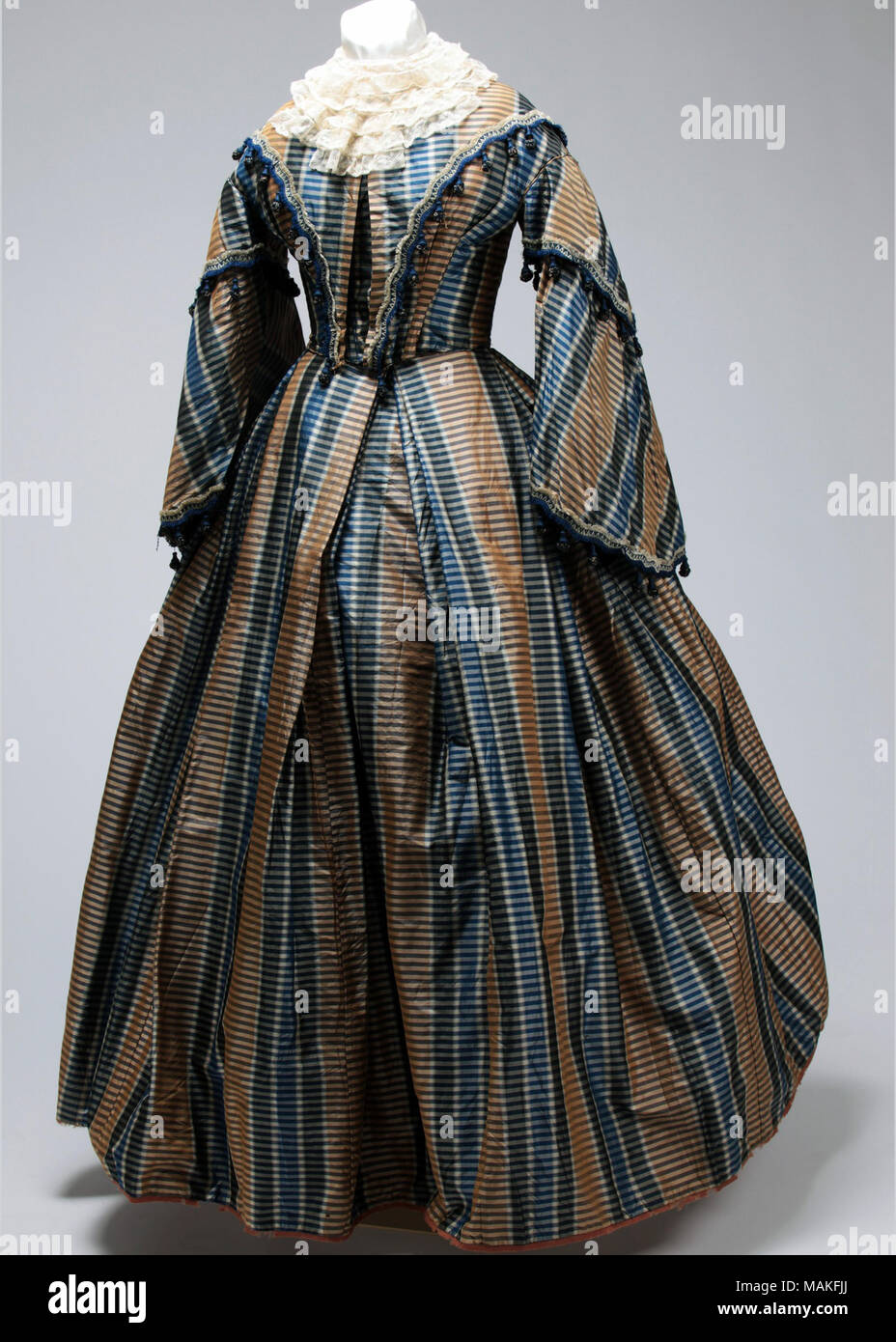Woman's blue, brown and cream striped taffeta two-piece dress with close fitting bodice, pagoda sleeves, and full skirt. Title: Woman's Two-Piece Striped Taffeta Evening Gown  . between circa 1853 and circa 1856. Stock Photo