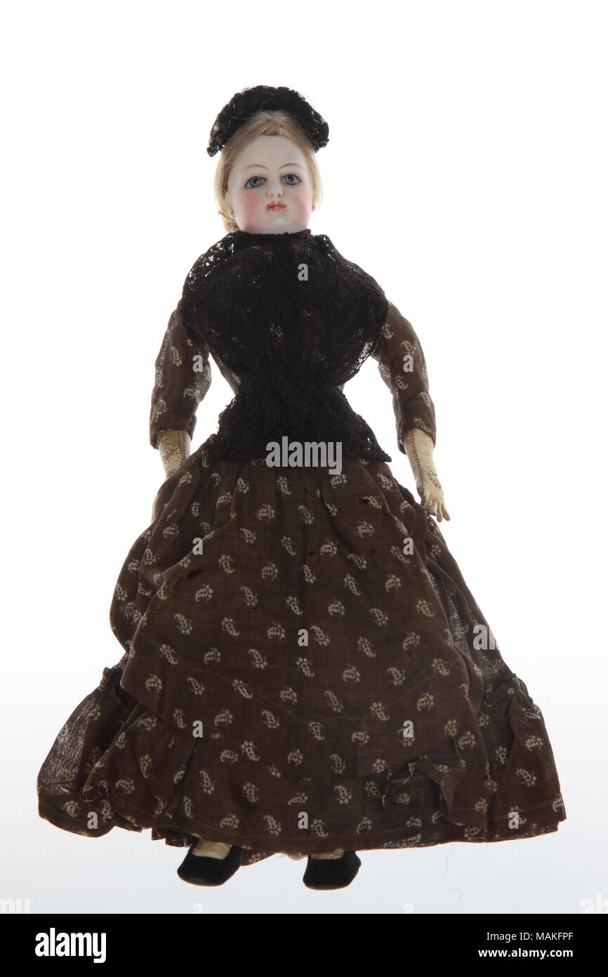 French fashion bisque doll has swivel head with kid body, hands and feet. She is wearing a brown and white paisley print dress. Title: French Fashion Bisque Doll with Brown and White Paisley Dress  . circa 1855. Stock Photo
