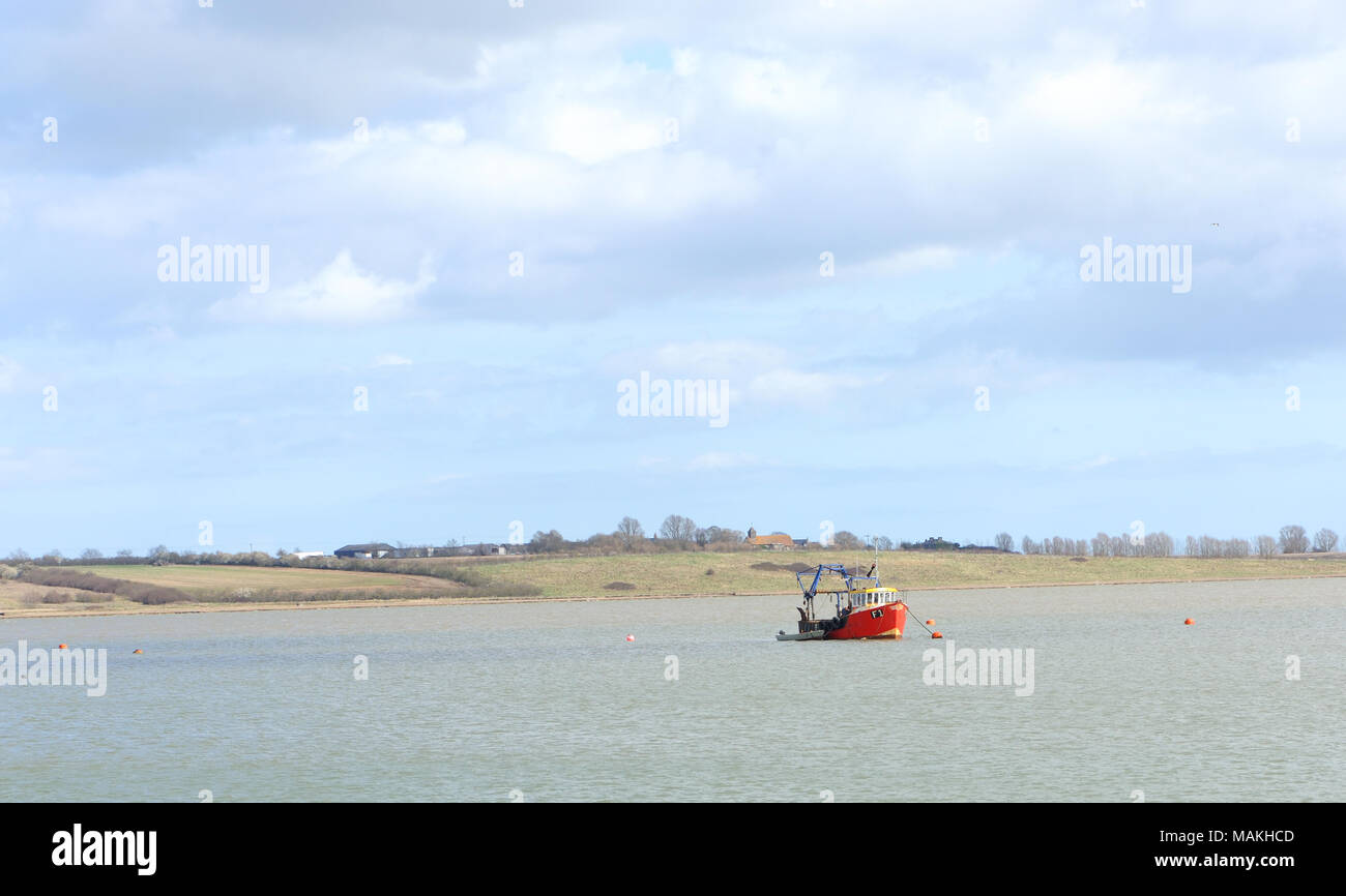 A fishing boat anchored in the Swale. The Isle of Sheppey in the background with the church of St Thomas the Apostle in the hamlet of Harty. Stock Photo