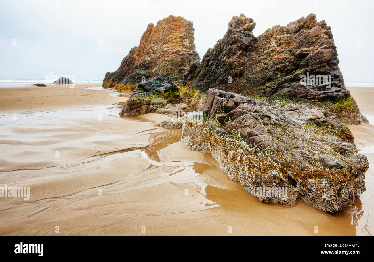 At low tide, on a wet spring day, intertidal rocks loom under low ceiling clouds at Hug Point near Cannon Beach on the Oregon Coast. Stock Photo