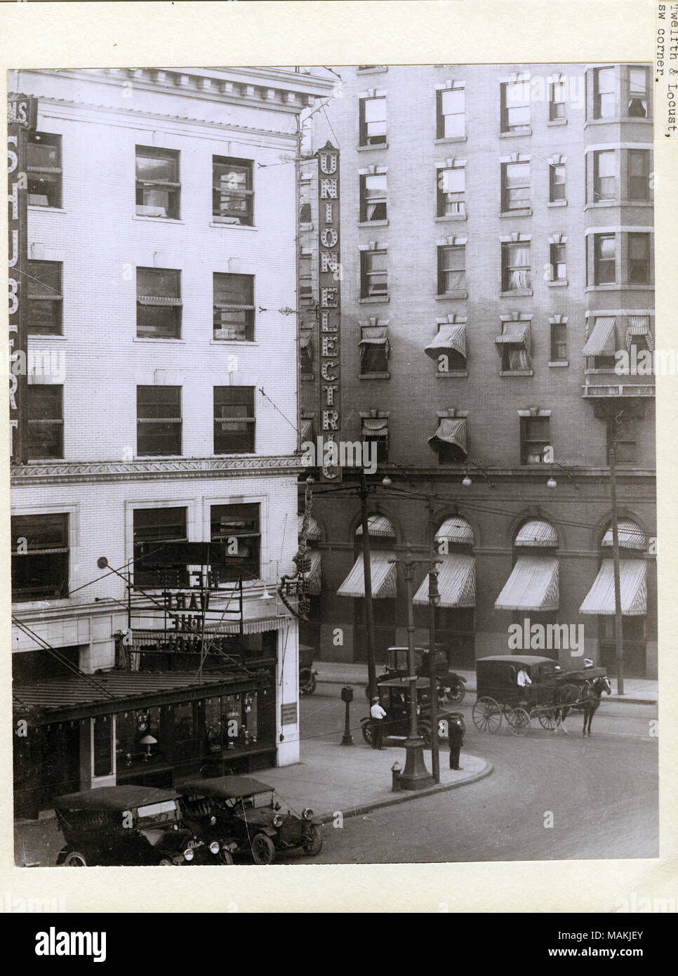 Vertical, black and white photograph showing the Union Electric Building on the southwest corner of Locust and 12th Street, now Tucker Boulevard. An electric 'Union Electric' sign is attached to the side of the building. Several cars are parked along the curb, and a horse-drawn carriage or buggy is driving along the street. Along the right edge, a sign can be seen for the Shubert Theatre. Title: Union Electric Building on the southwest corner of Locust and 12th Street, now Tucker Boulevard.  . circa 1910. Holt, Charles Clement, 1866-1925 Stock Photo