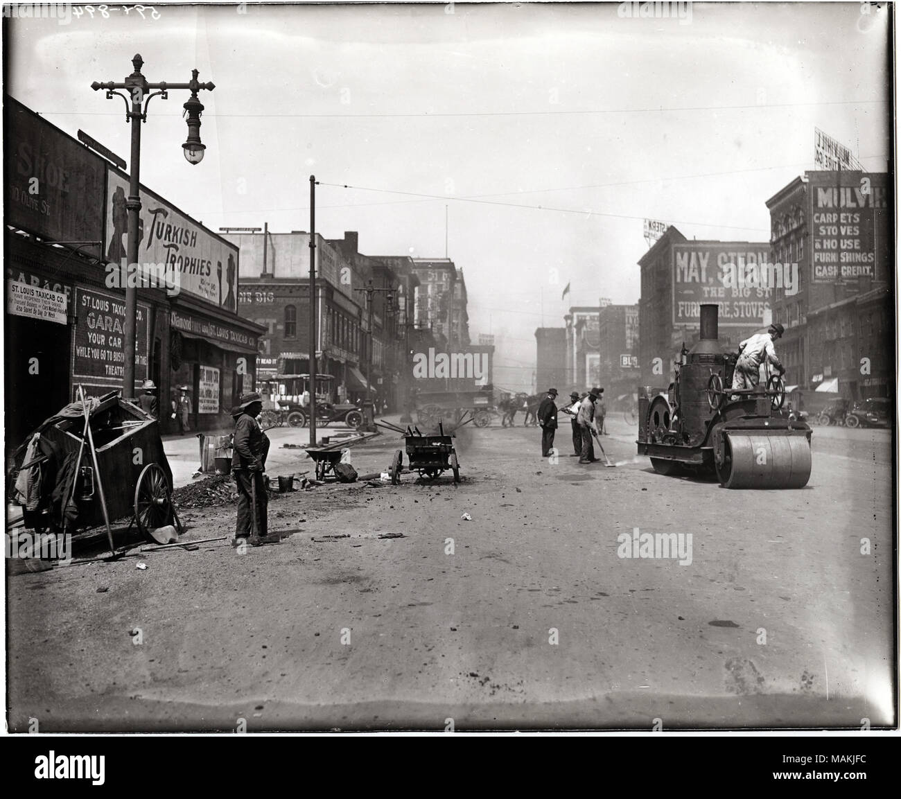 Horizontal, black and white photograph showing workers repaving 12th  Street, now Tucker Boulevard, just south of Chestnut. Workers are using a  large roller to smooth the asphalt, as well as a variety