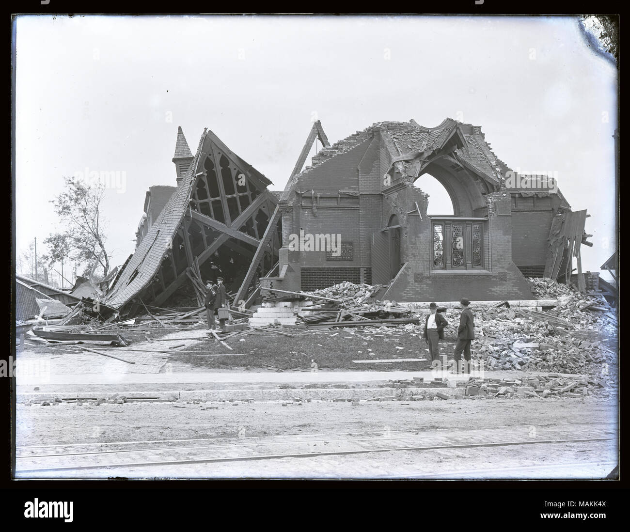 Horizontal, black and white photograph showing the Mount Calvary Protestant Episcopal Church, probably after the 1896 tornado. The building is destroyed: the roof lies on the ground, exterior walls are knocked down, and windows are missing. Piles of rubble are strewn throughout the photograph. Four men are standing at the scene. Title: Destruction at the Mt. Calvary Protestant Episcopal Church, probably after the 1896 tornado.  . 1896. Stock Photo