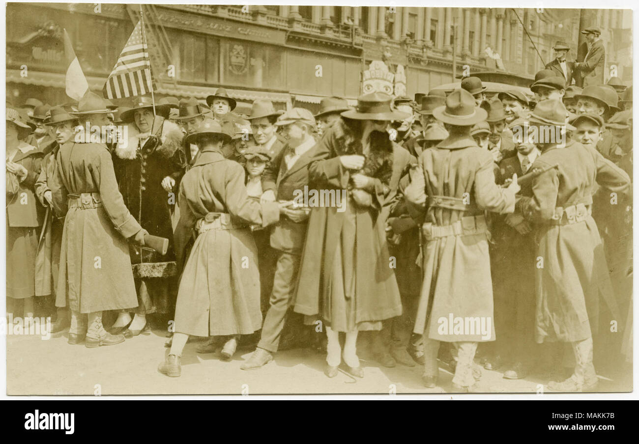 Horizontal, sepia photograph showing four uniformed soldiers attempting to hold a crowd of civilians back from a given area, possibly for a parade. The surrounding buildings suggest a downtown area, and the top of a streetcar can be seen behind the crowd. Title: Crowd Being Held Back By Four Uniformed Soldiers, Possibly for a Parade.  . between circa 1914 and circa 1918. Michel, Carl Stock Photo