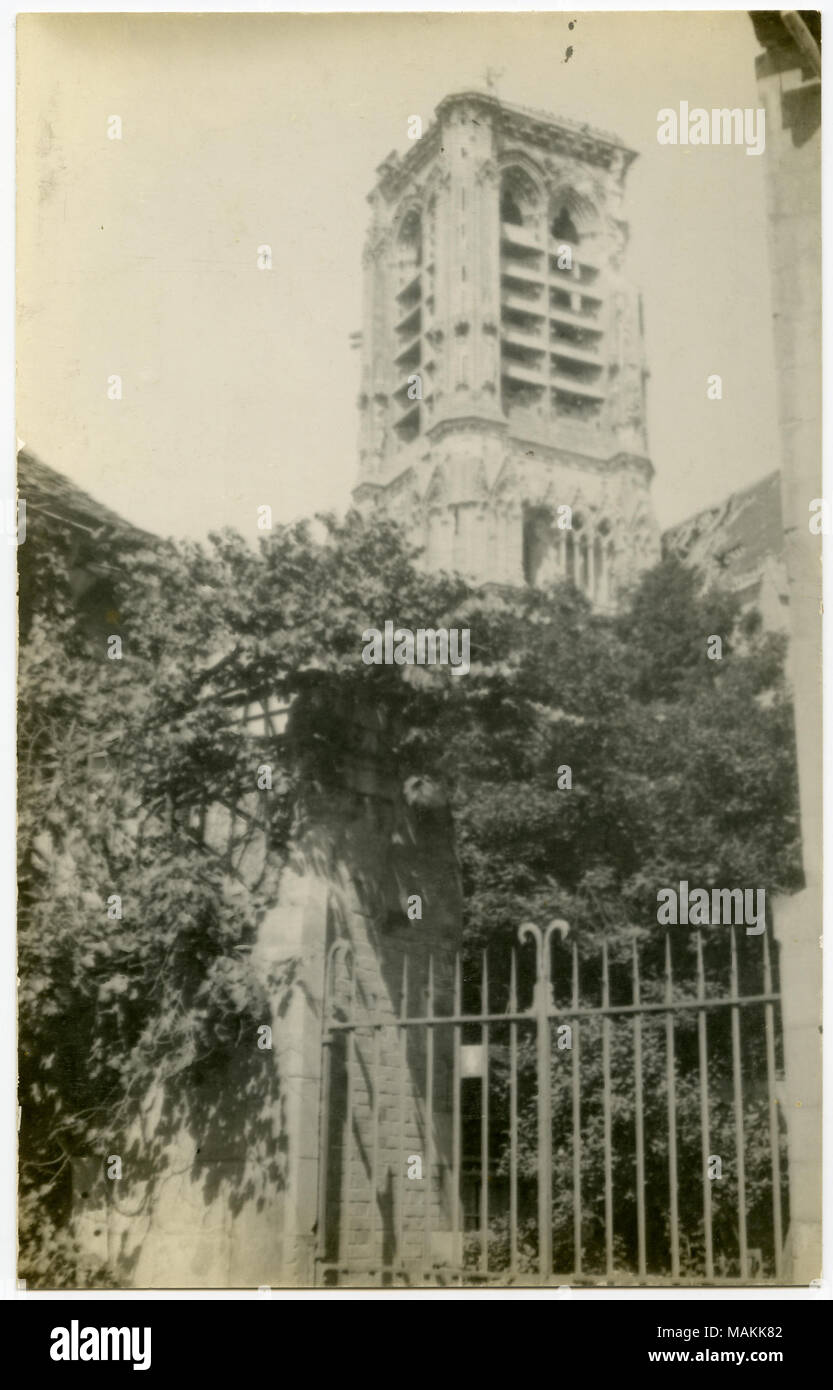 Vertical, sepia photograph showing a brick pillar and a gate leading to a tree-covered area. A tower, possibly a church tower, is situated near the gated area. Title: A Church Tower Situated Near a Gated Area With Trees Inside.  . between circa 1914 and circa 1918. Michel, Carl Stock Photo