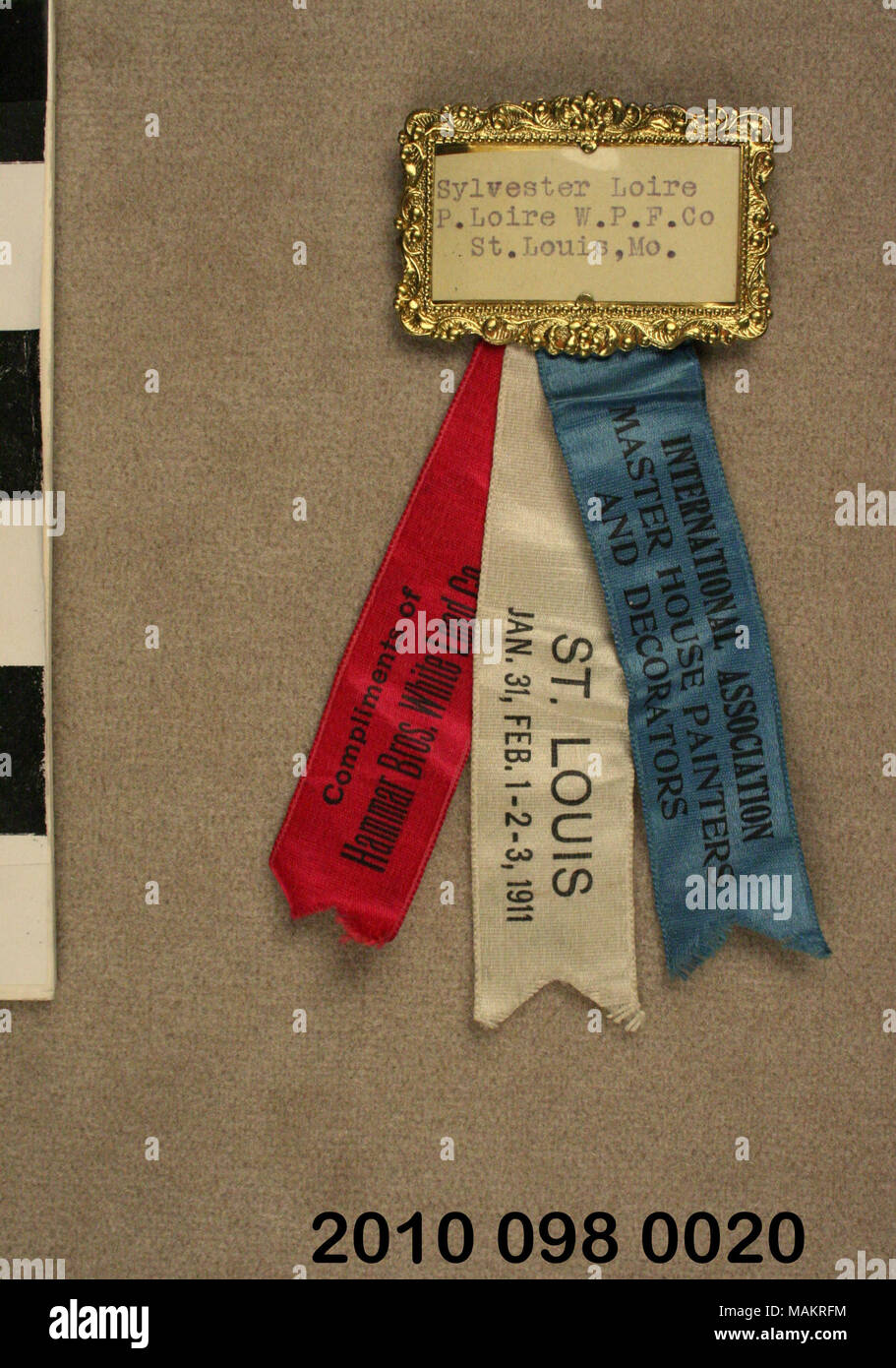 Badge of Sylvester Loire from the International Association of Master House Painters and Decorators convention in St. Louis in 1911. Brass frame with Loirs's name typed on paper and three ribbons hanging below. Title: House Painters and Decorators Convention Badge for Sylvester Loire  . 1911. Stock Photo
