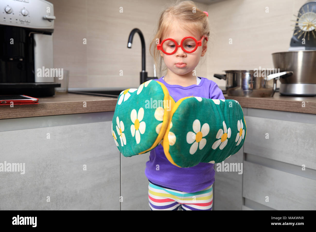 Kid with kitchen mittens. Funny little girl wearing big kitchen gloves. Stock Photo
