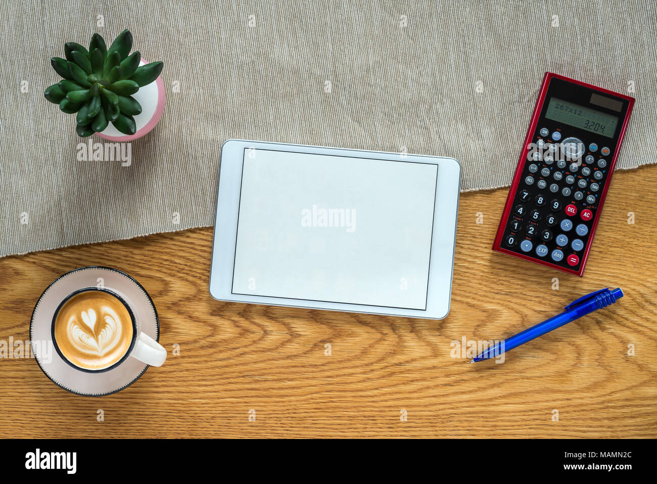 Accountant workspace as flat lay from above with blank tablet screen and calculator, plant and coffee with wooden background Stock Photo