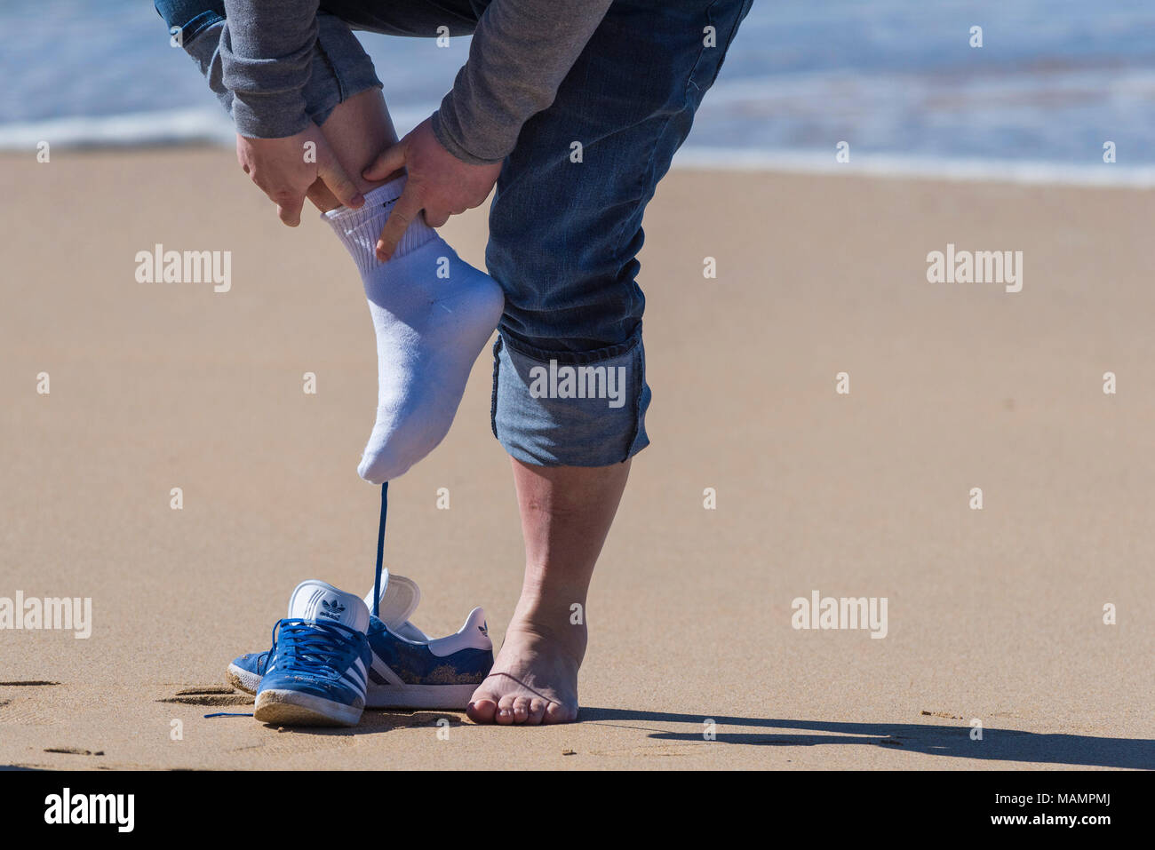 A holidaymaker taking off his shoes and socks on Fistral Beach in Newquay, Cornwall. Stock Photo