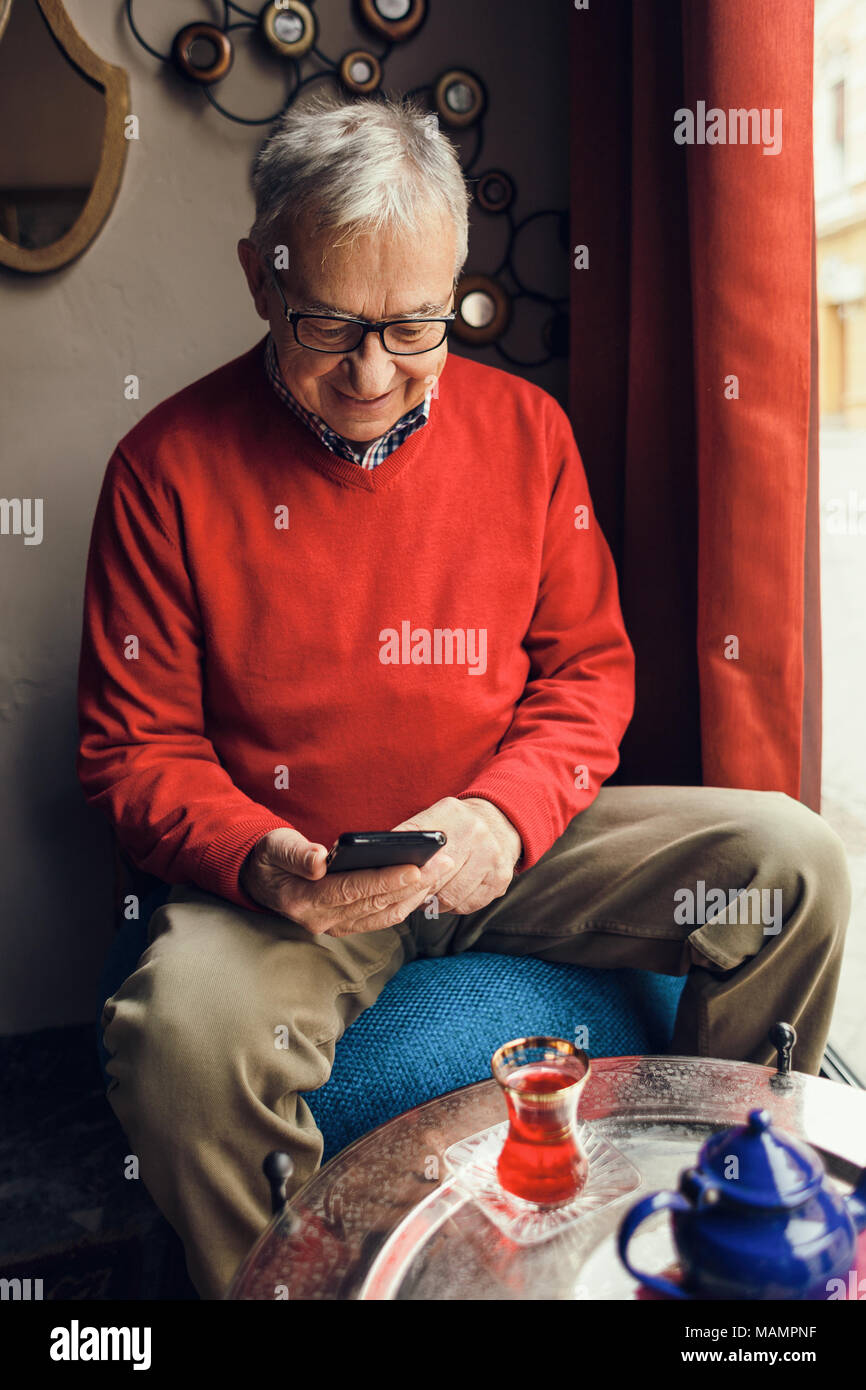 Senior man is sitting in cafe and typing message on mobile phone. Stock Photo