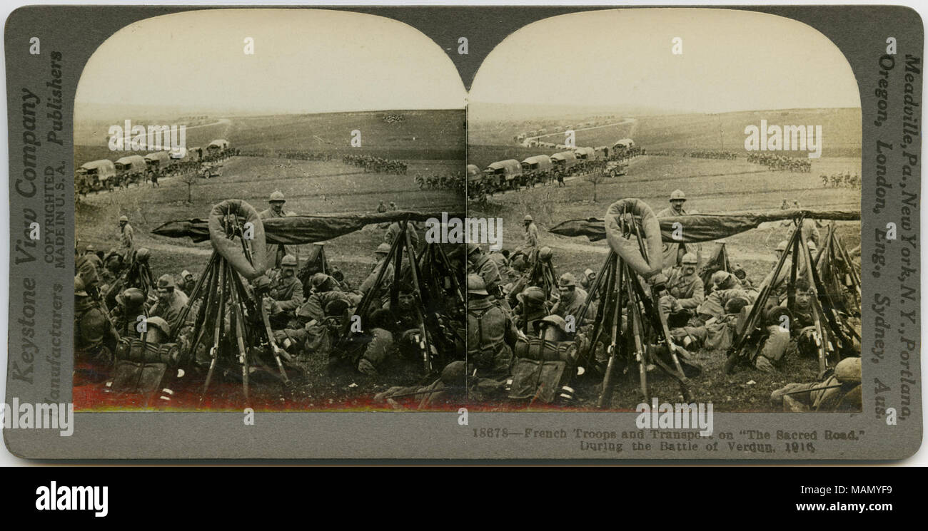 Horizontal, sepia stereocard showing French troops in uniform resting in a field. A road filled with caravans of supplies and uniformed men can be seen in the background. Keystone Stereograph number 18678. The title reads: 'French Troops and Transport on 'The Sacred Road,' During the Battle of Verdun, 1916.' Title: 'French Troops Resting After a Combat with 'Fritz' '  . 1916. Keystone View Company Stock Photo