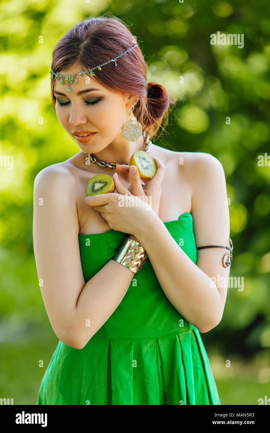 Portrait of a beautiful young asian woman holding two halves of kiwi ...