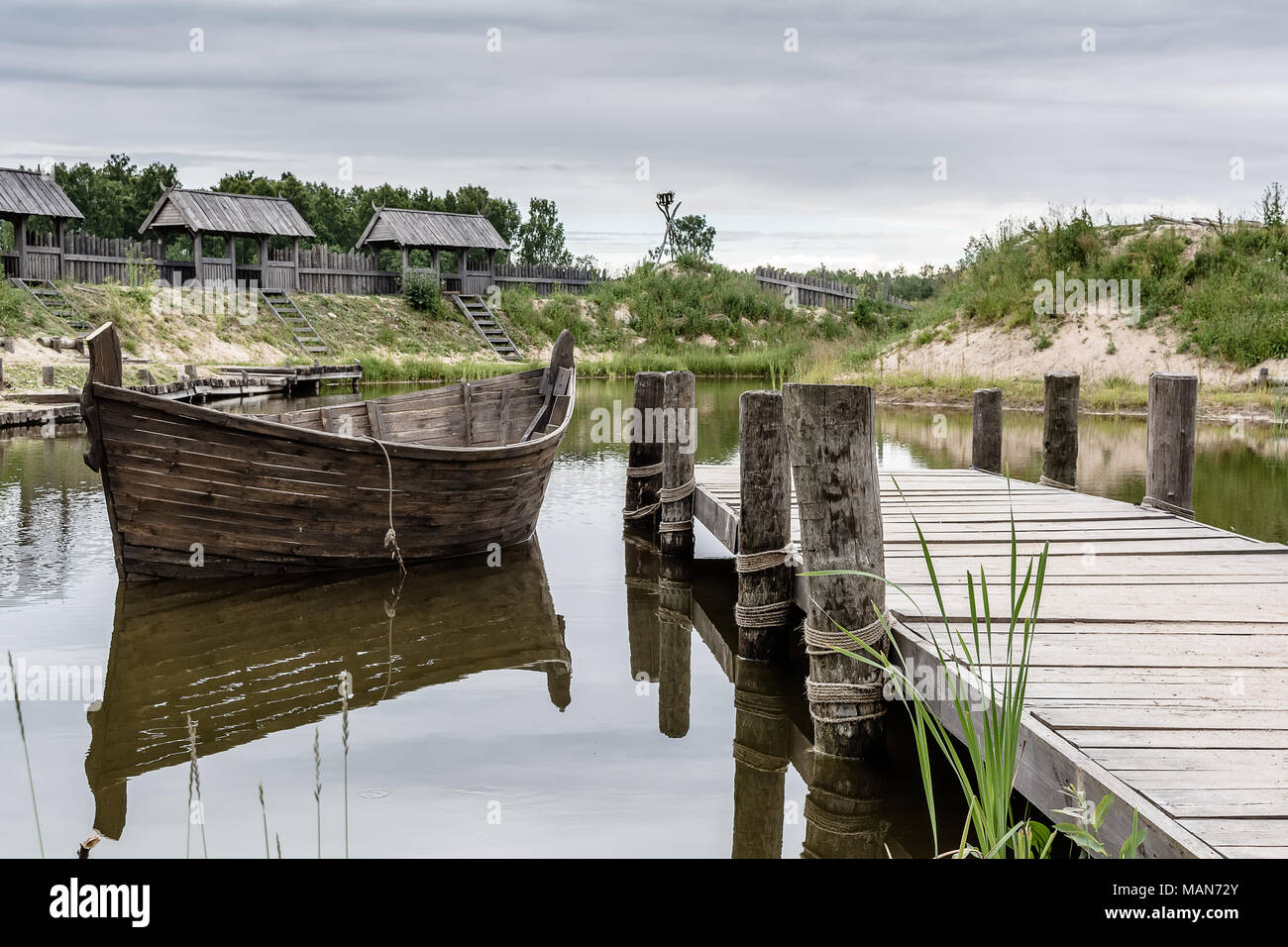 Tukums region, Latvia - July 8 2017: Medieval scenery near the lake with boat and wooden wall reflected in the water. Stock Photo