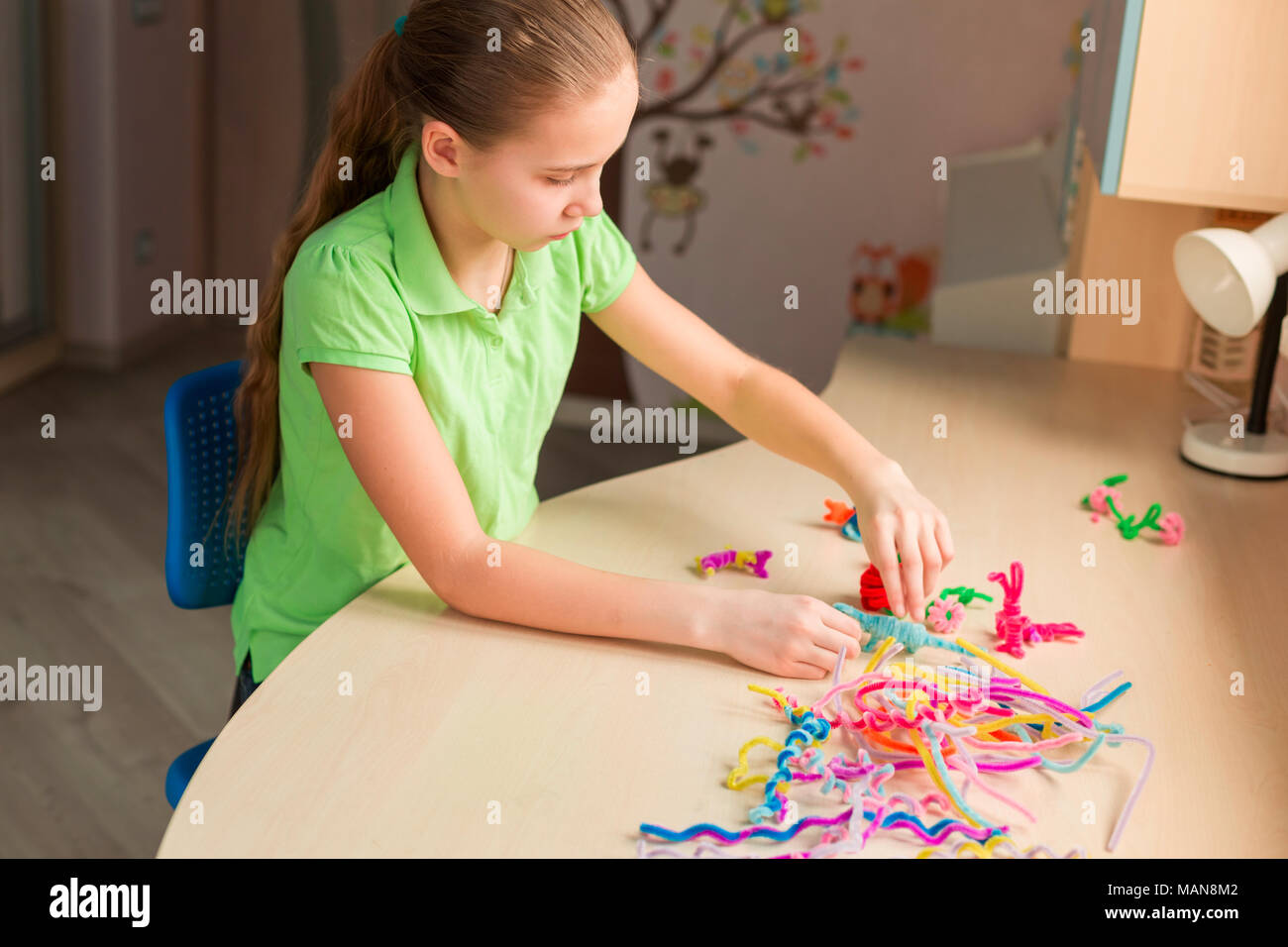 Cute little girl creating toys with chenille sticks at the table. Creativity and handmade concept. Stock Photo