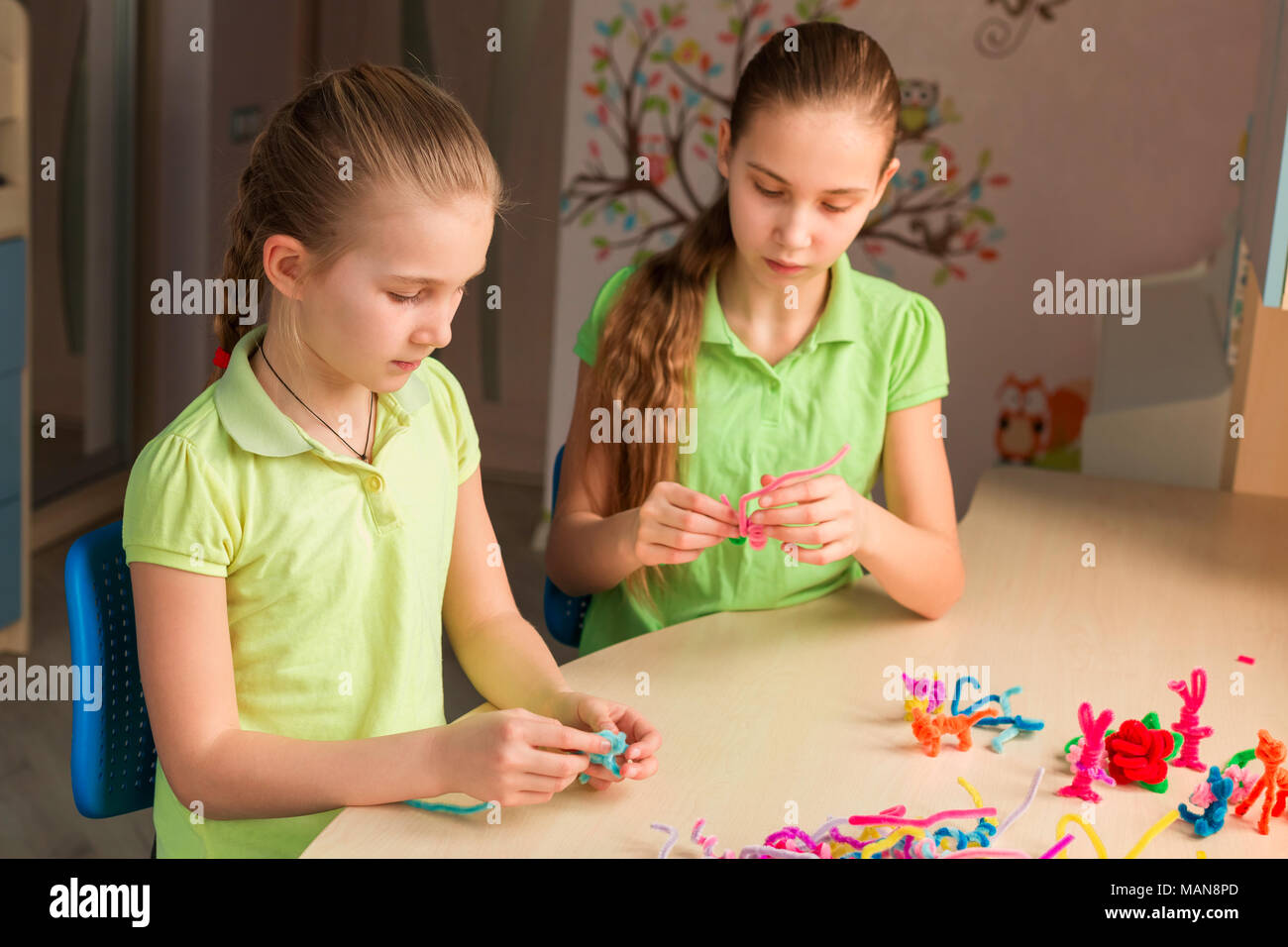 Cute little girls creating toys with chenille sticks at the table. Creativity and handmade concept. Stock Photo