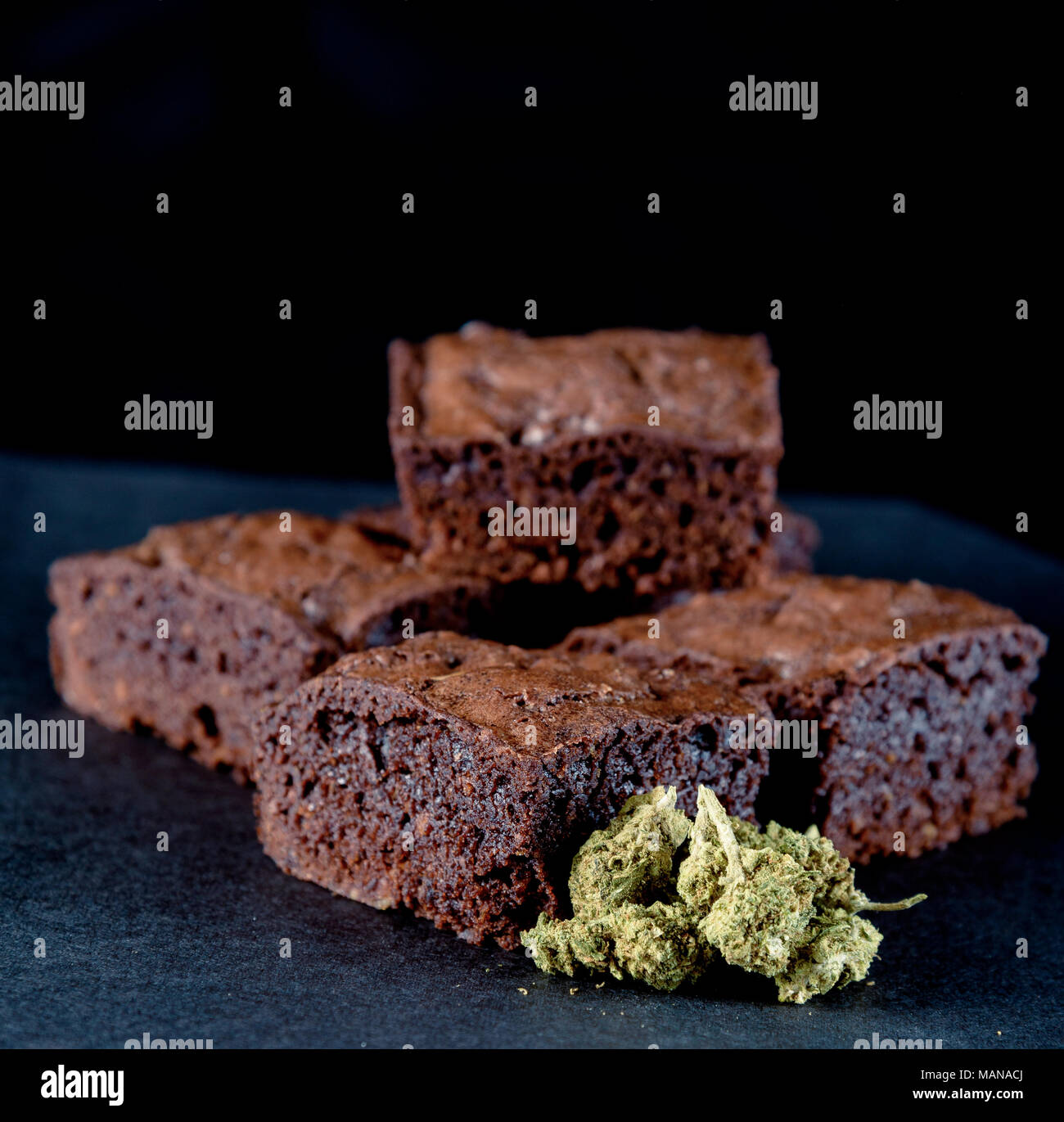 A stack of marijuana edible brownies next to a small pile of medical marijuana nugs. Black background Stock Photo