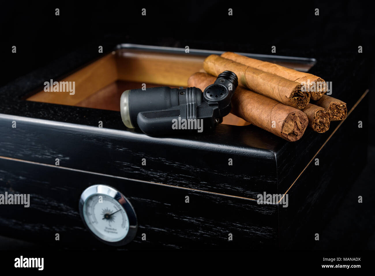a black butane torch and a pile of fresh cigars above a black humidor. Black background Stock Photo