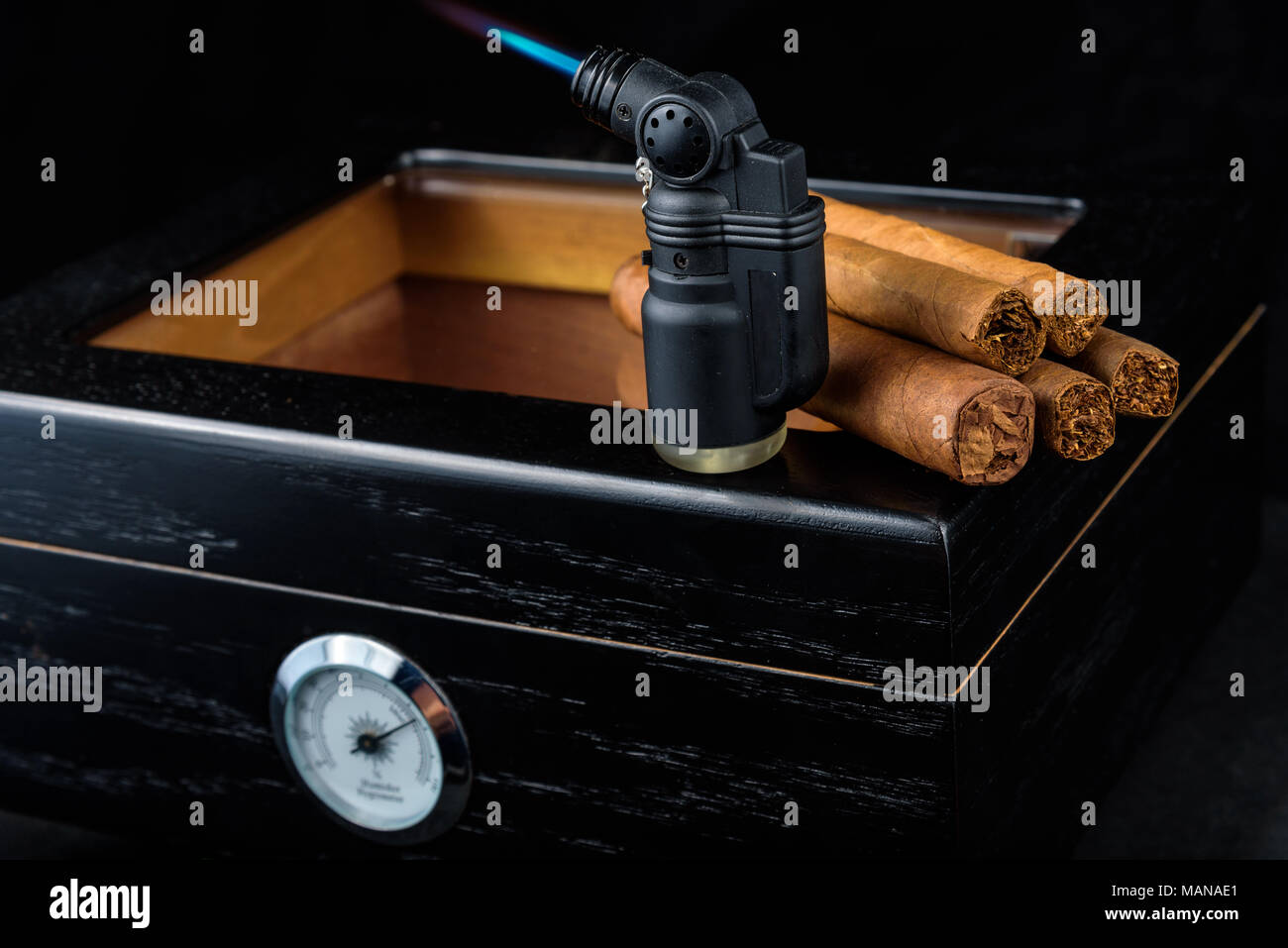 a lit black butane torch and a pile of fresh cigars above a black