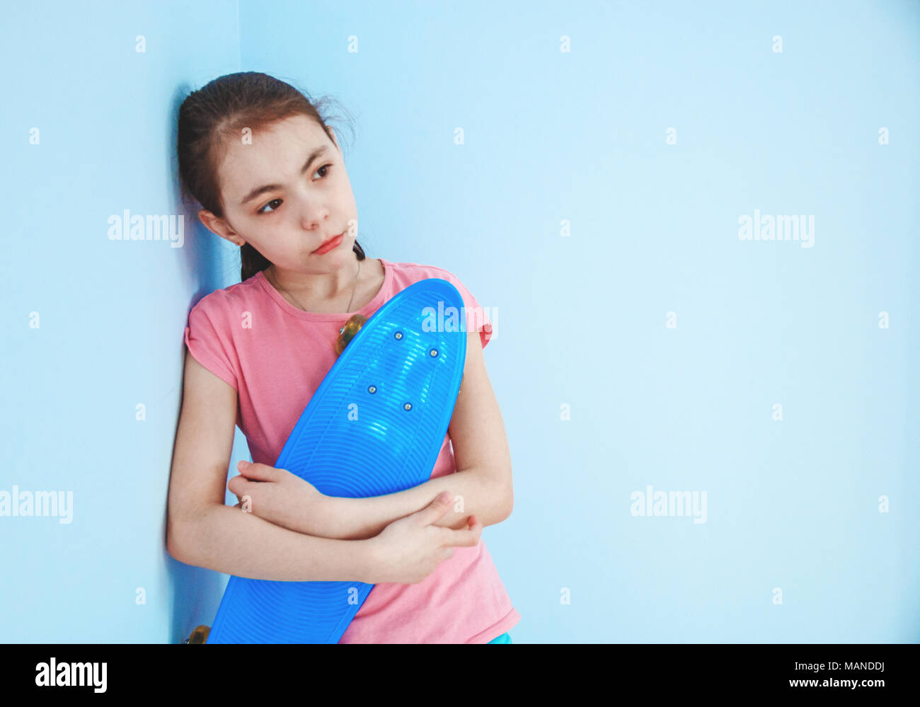 sad girl standing by the wall holding in his hand a blue skate. Stock Photo