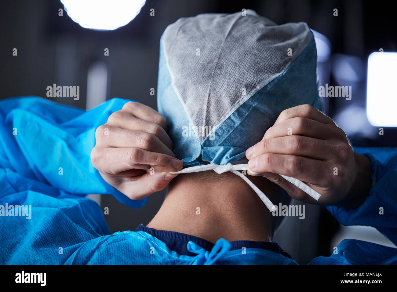 Surgeon tying surgical cap in preparation, back view Stock Photo