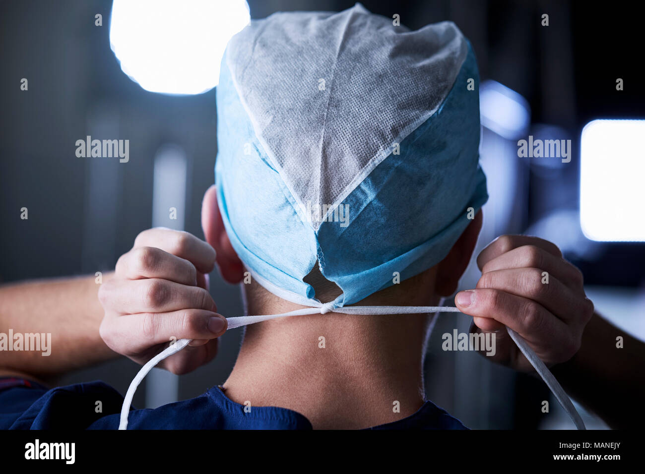Surgeon tying surgical cap in preparation, back view Stock Photo