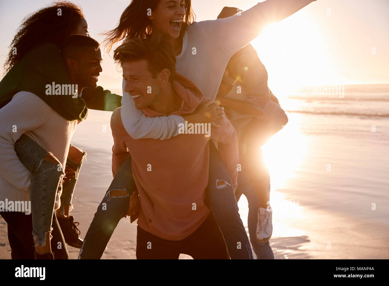 Group Of Friends Having Piggyback Race On Winter Beach Together Stock Photo