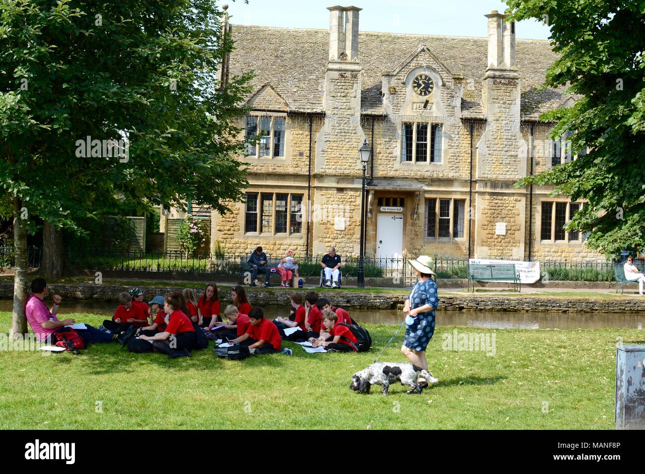 School children enjoying a lesson outdoors, the river windrush is in the background,  Bourton on the water, Gloucestershire, UK Stock Photo