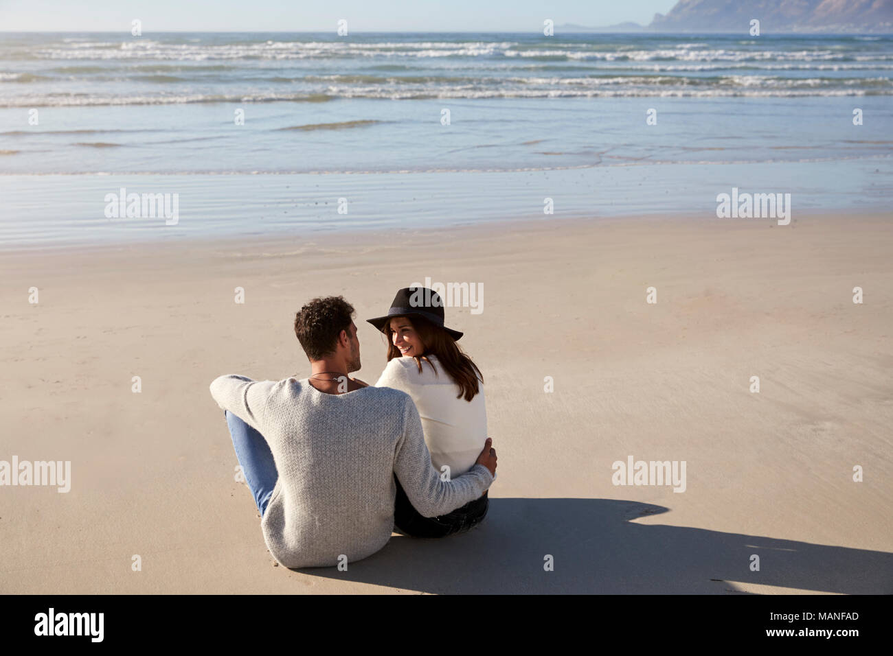 Romantic Couple Sitting On Winter Beach Together Stock Photo