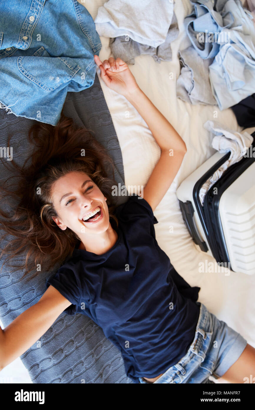 Overhead View Of Woman Lying On Bed Packing For Vacation Stock Photo