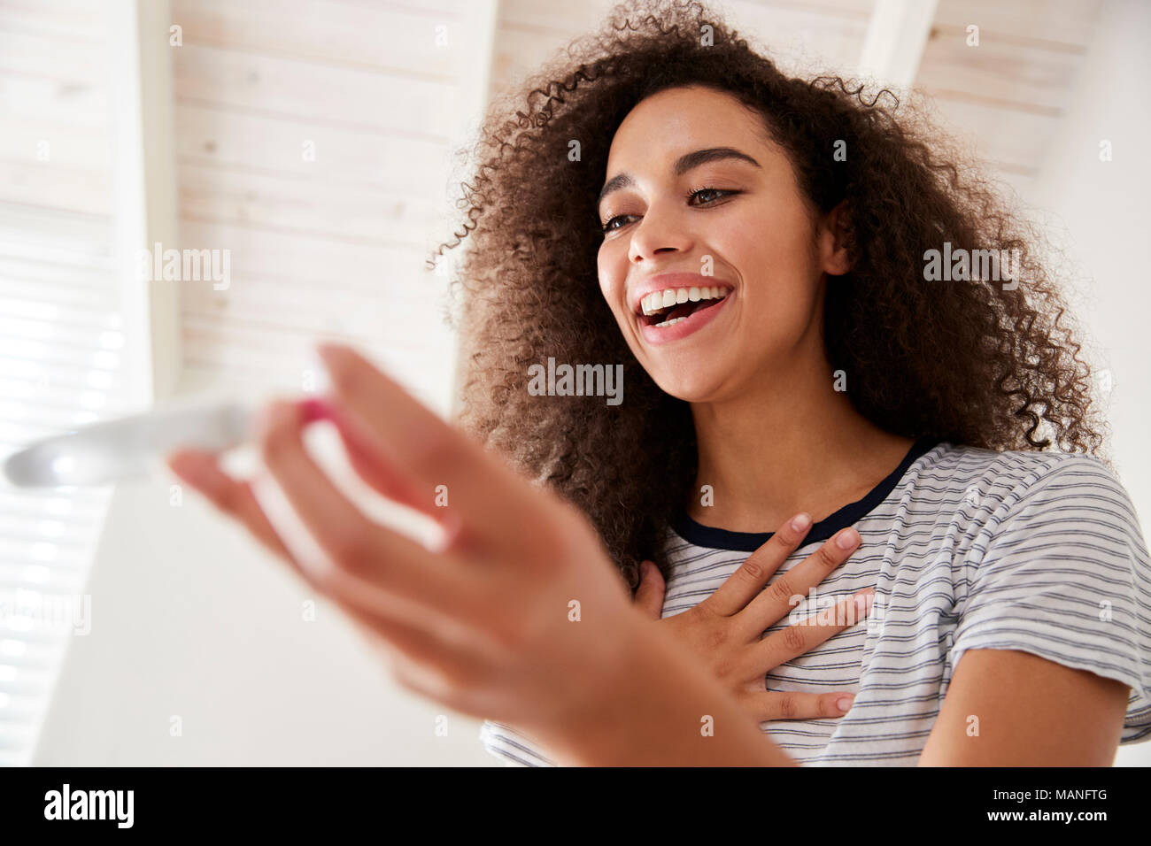 Woman In Bathroom Celebrates Positive Home Pregnancy Test Result Stock Photo
