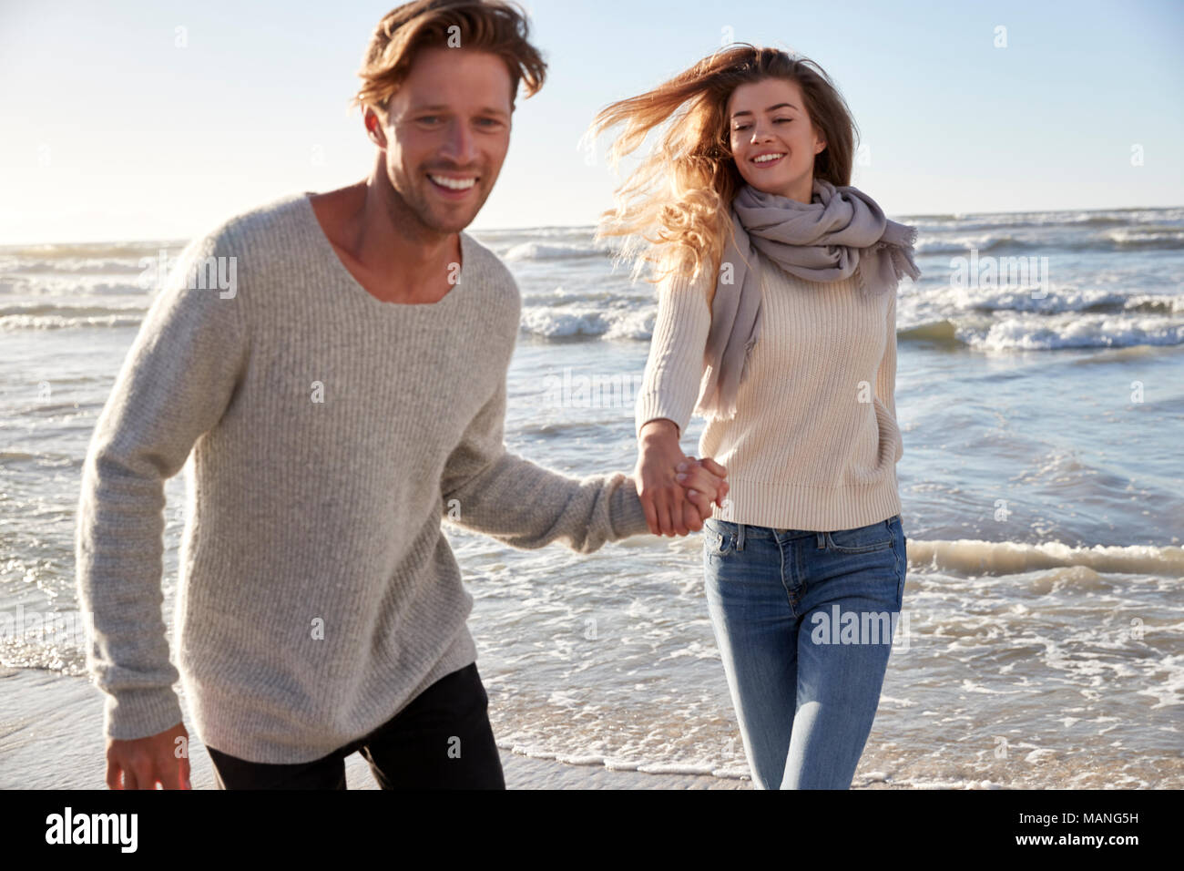 Couple Having Fun Running Along Winter Beach Together Stock Photo