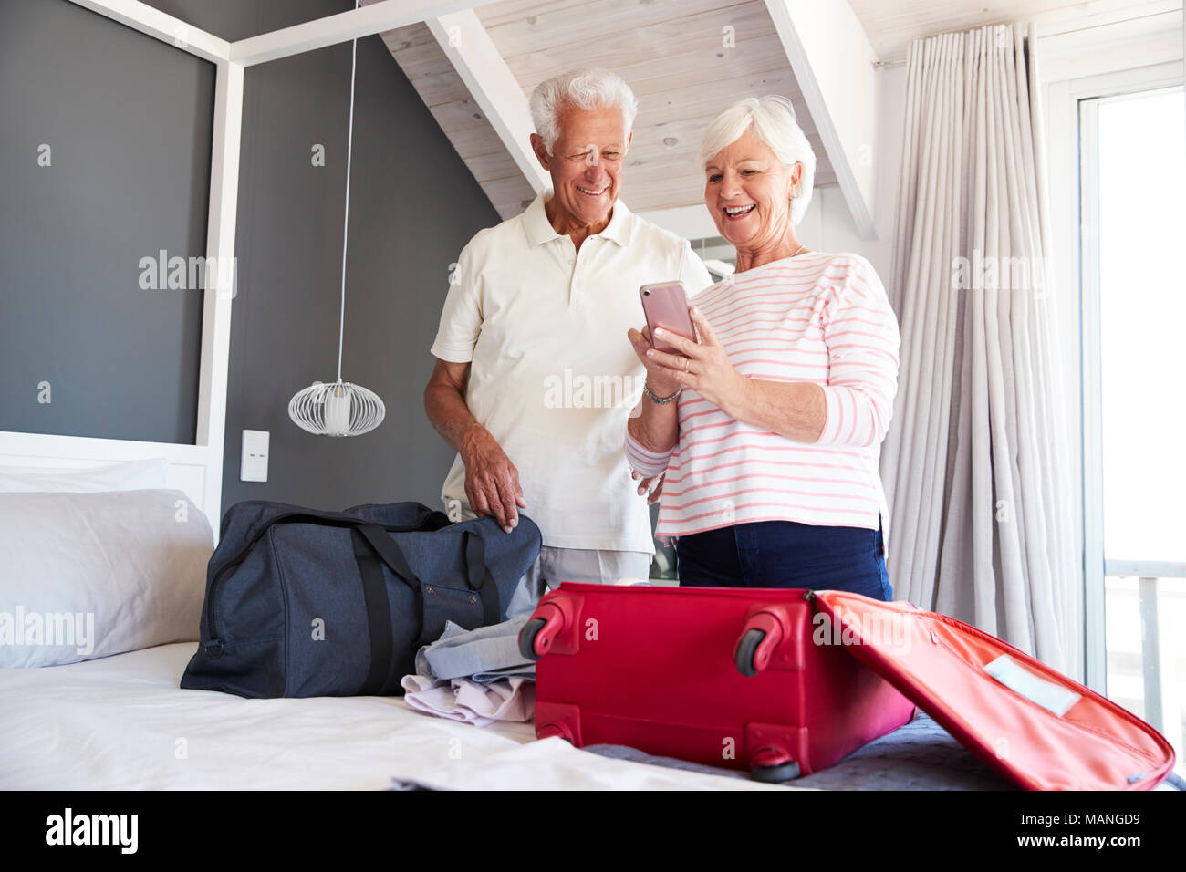 Senior Couple Look At Mobile As They Check In To Vacation Rental Stock Photo