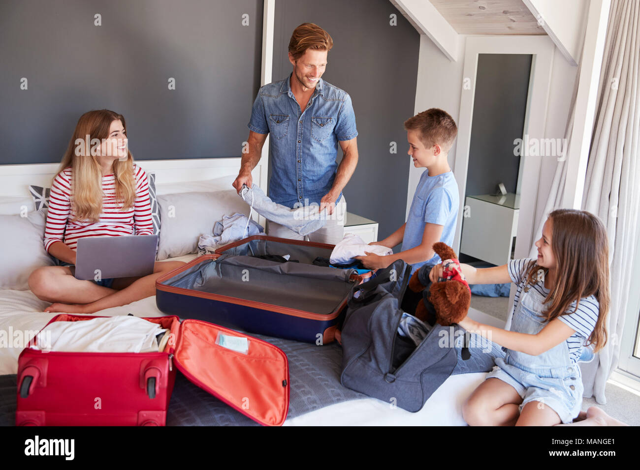 Family In Bedroom Pack Suitcases For Vacation And Use Laptop Stock Photo