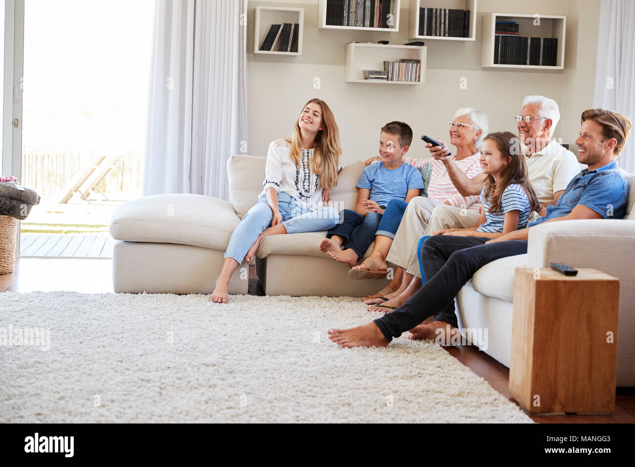 Multi Generation Family Sitting On Sofa At Home Watching TV Stock Photo